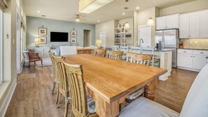 Una cocina amplia con armarios blancos, una gran mesa de comedor de madera y un refrigerador empotrado.