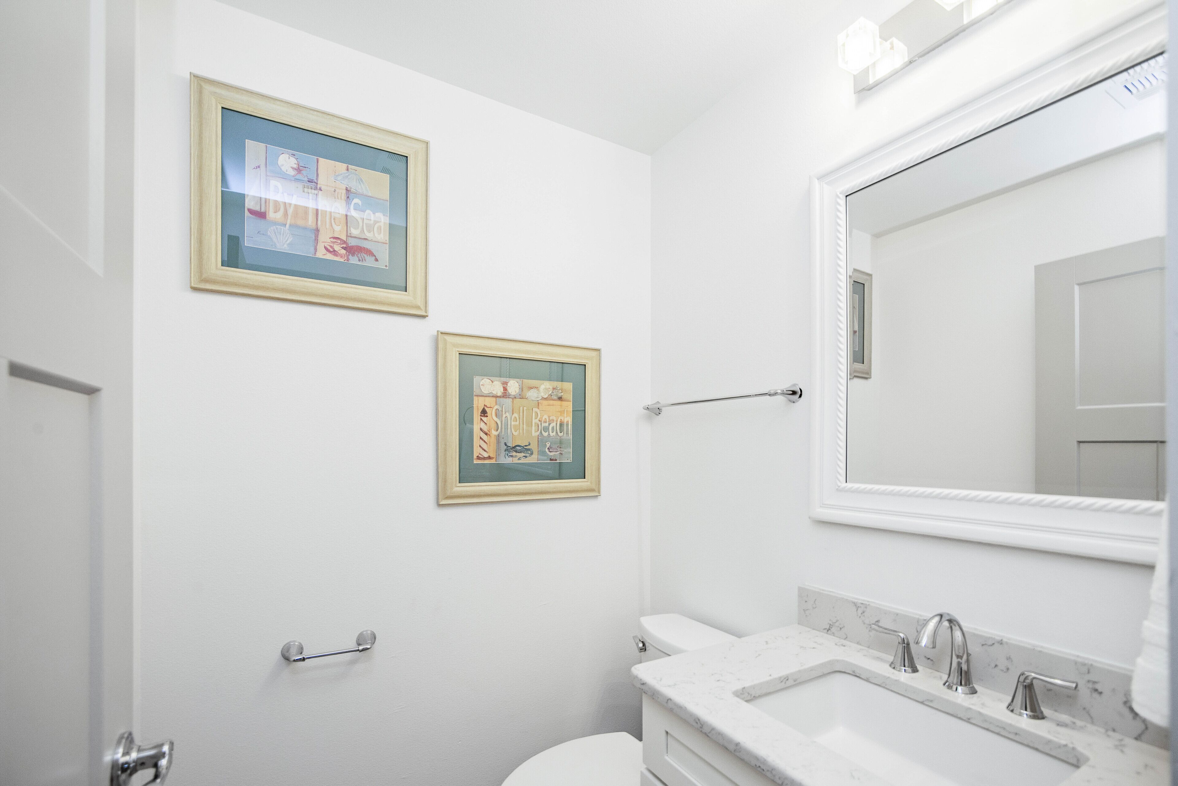 Un baño con un lavamanos blanco, un espejo y dos cuadros en la pared.