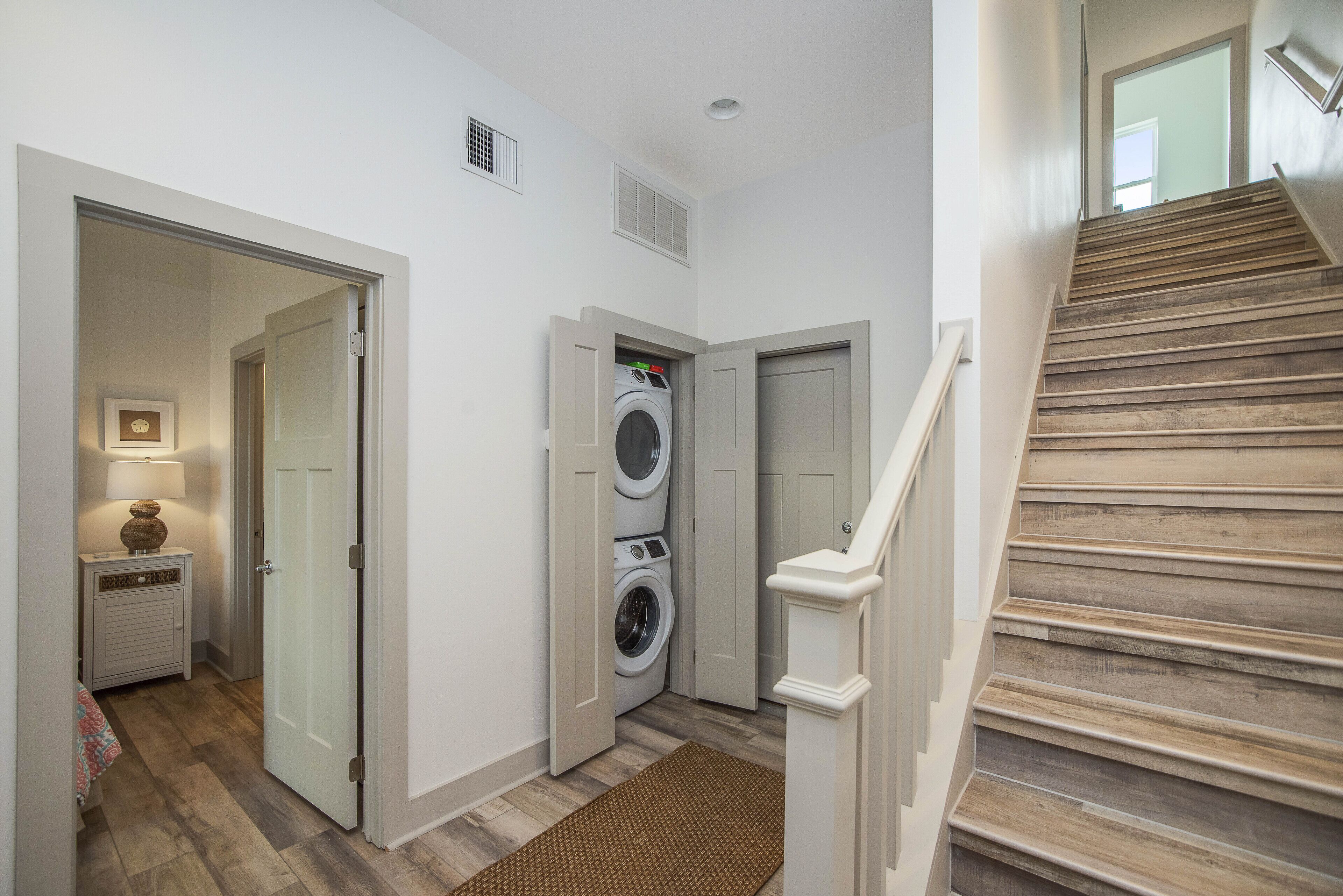 A laundry room with a washing machine and dryer, a wooden staircase, and a hallway with a rug.