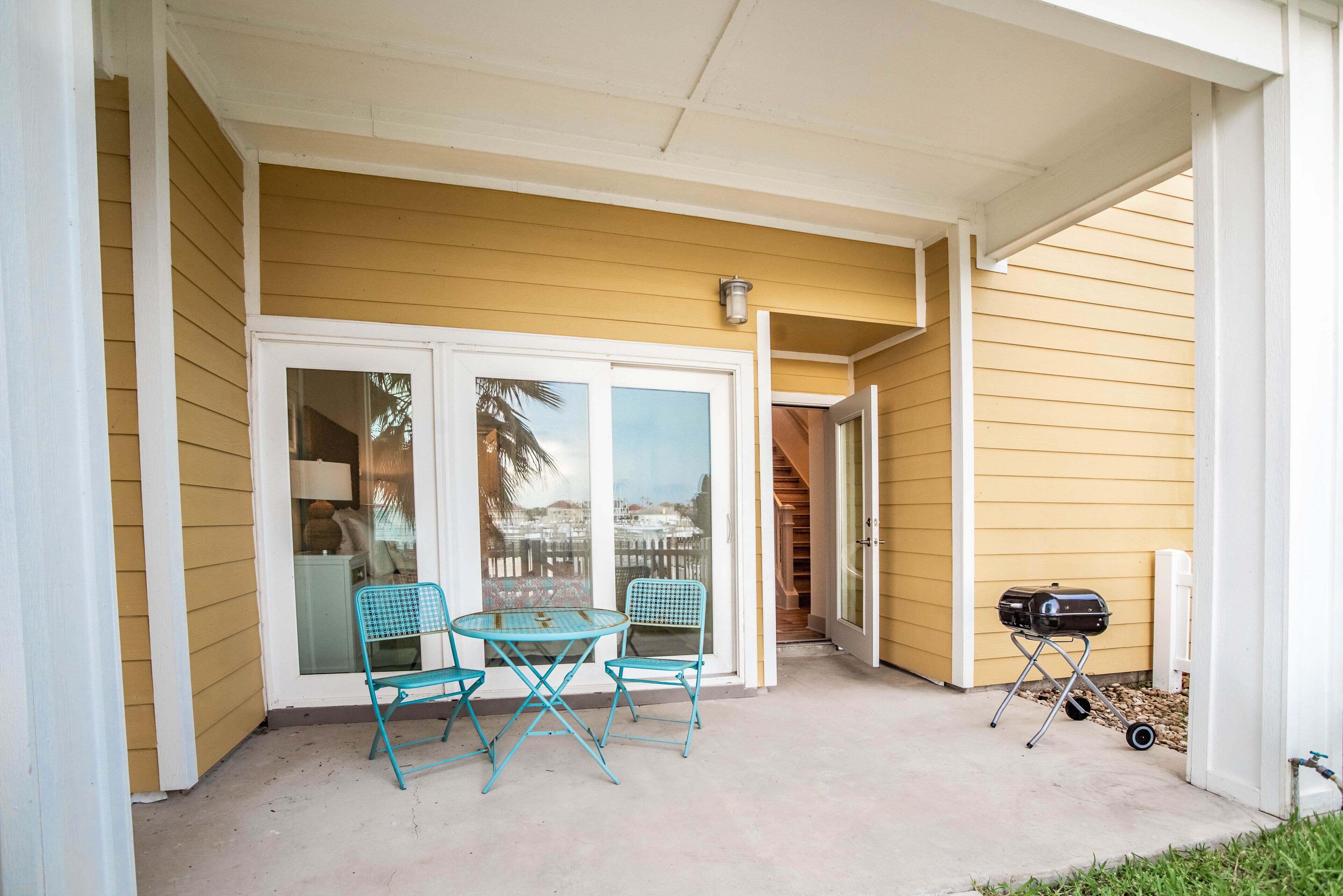 A covered patio with a table and chairs, a grill, and a view through glass doors.