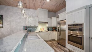 A modern kitchen with white cabinets, stainless steel appliances, and a marble countertop. - Marina Del Bell - Elevator! Boat Slip for Rent! (Port Aransas)