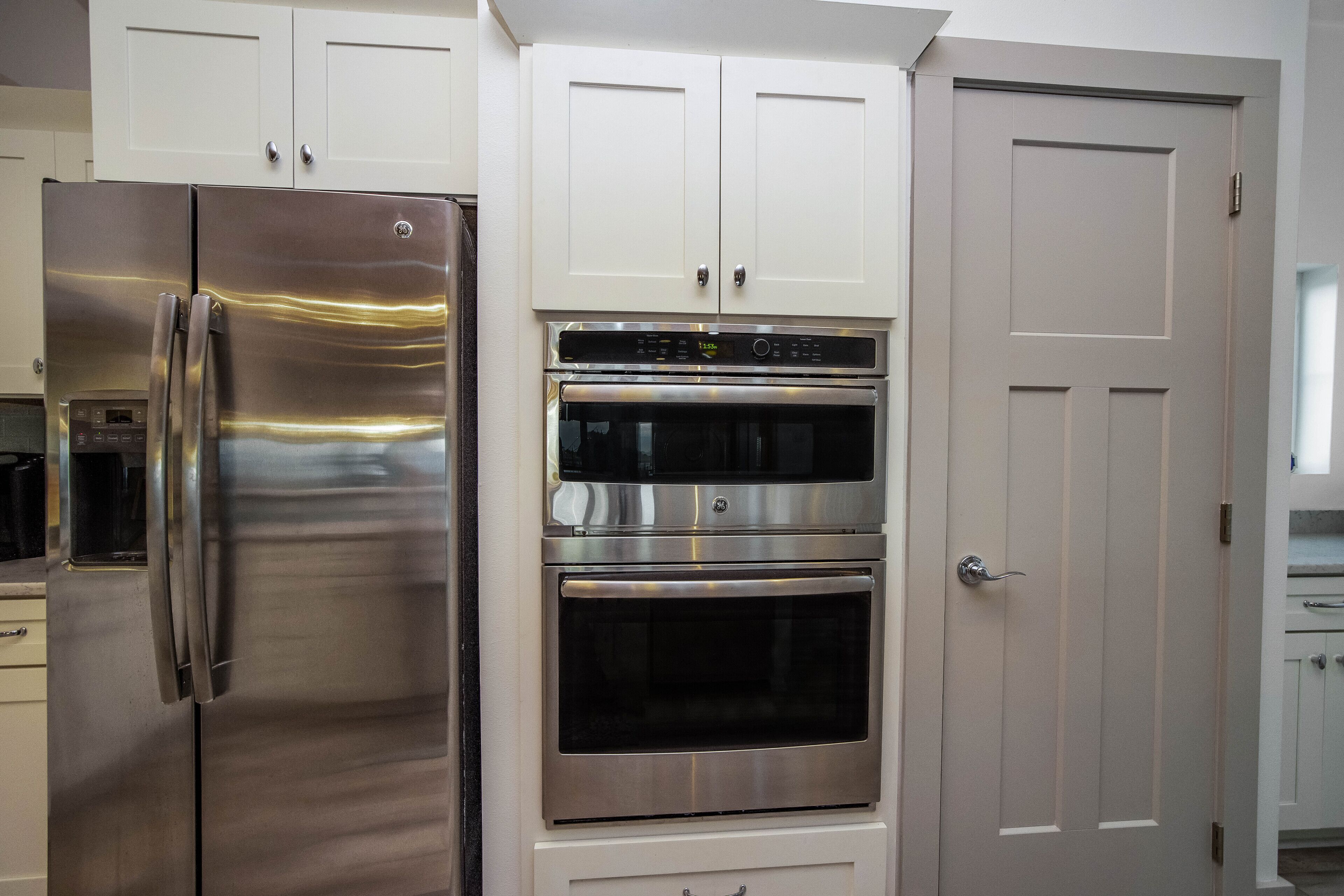A kitchen with a stainless steel refrigerator, a double oven, and white cabinetry.