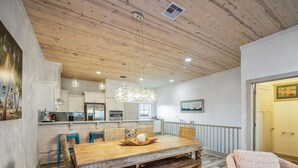 A spacious living area with a wooden dining table, blue chairs, and a large window. - Marina Del Bell - Elevator! Boat Slip for Rent! (Port Aransas)