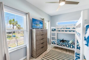 A room with a bunk bed, a wooden dresser, a television, and a window with blinds.