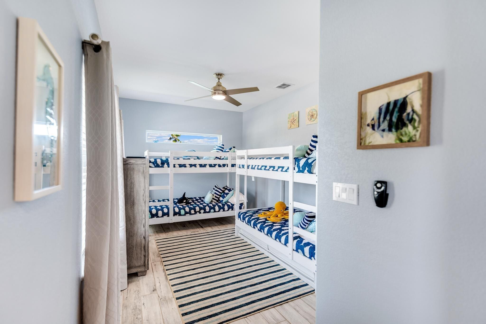 A room with bunk beds, a ceiling fan, a framed picture, and a window with a view.