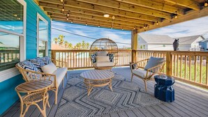 A covered outdoor deck with wicker furniture, a patterned rug, and a view of the surrounding area.