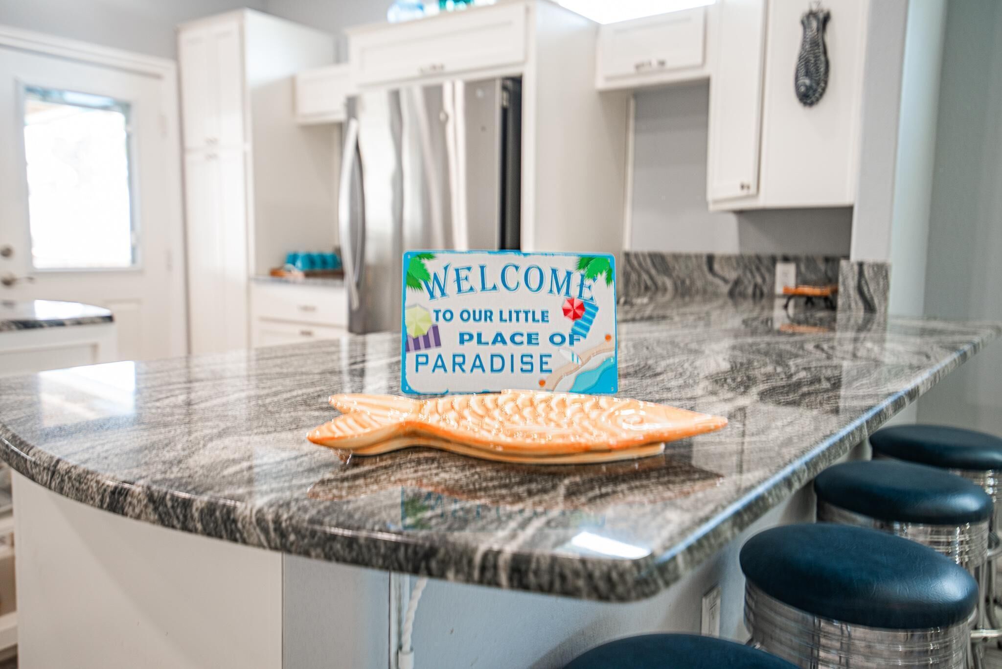 A kitchen with a marble countertop, a welcome sign, and bar stools.