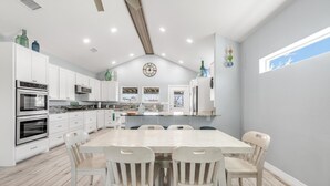 A modern kitchen with white cabinets, a large island, and a dining area with four chairs.