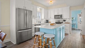 A modern kitchen with white cabinets, stainless steel appliances, and a blue island with stools. - Beachside Bliss - Beach Gear Credit Included! (Port Aransas)