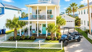A two-story house with a balcony, a front porch, and a golf cart parked in front. - Beachside Bliss - Beach Gear Credit Included! (Port Aransas)