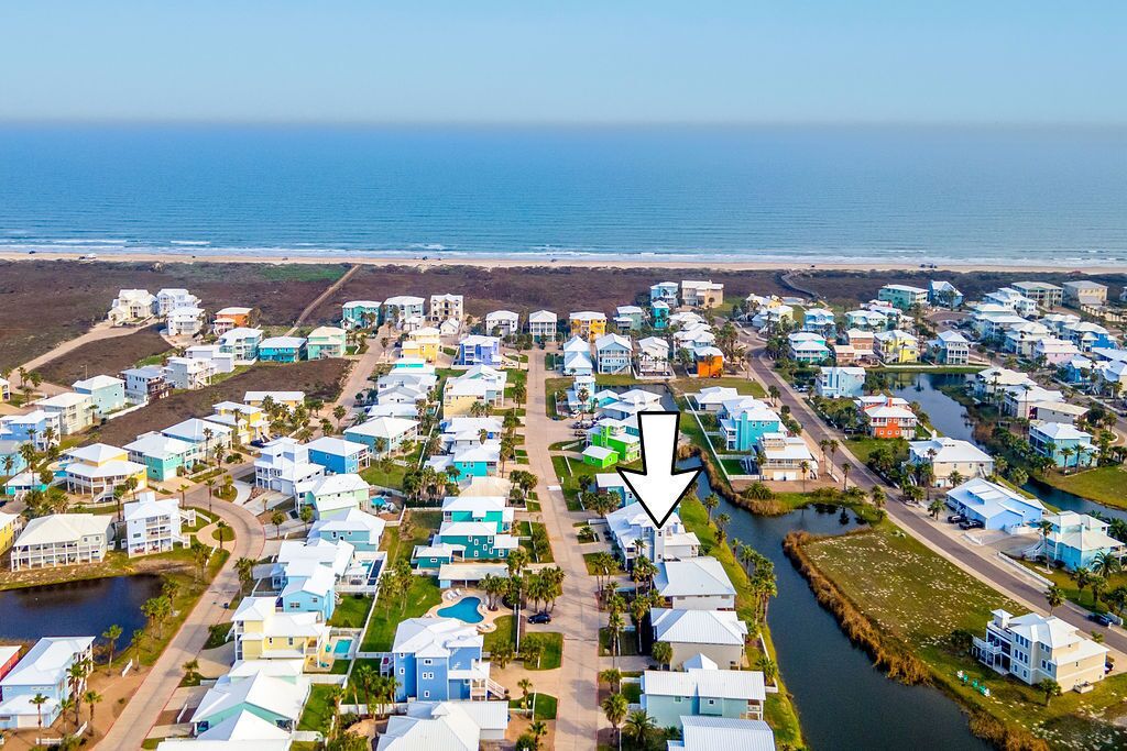 An aerial view of a coastal residential area with houses, a road, and a body of water.