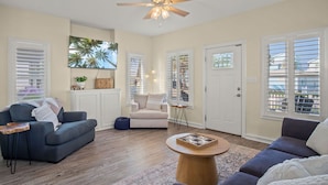 A spacious living room with a ceiling fan, two sofas, a coffee table, and a large window with blinds. - Beachside Bliss - Beach Gear Credit Included! (Port Aransas)