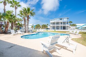 A pool area with white lounge chairs, a pool, and a two-story building with balconies.