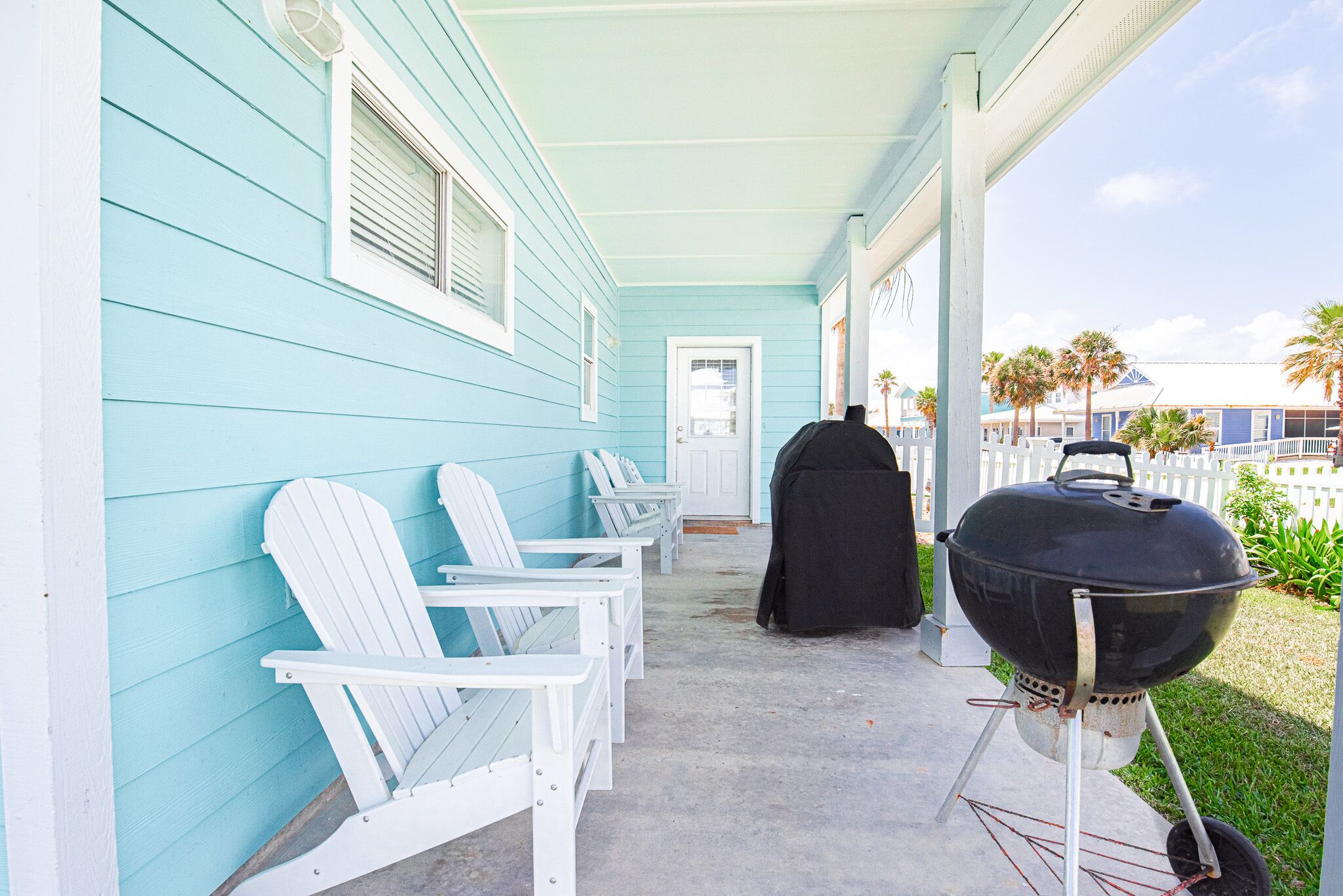 Un portico con poltrone Adirondack bianche, un barbecue nero e una casa azzurra.
