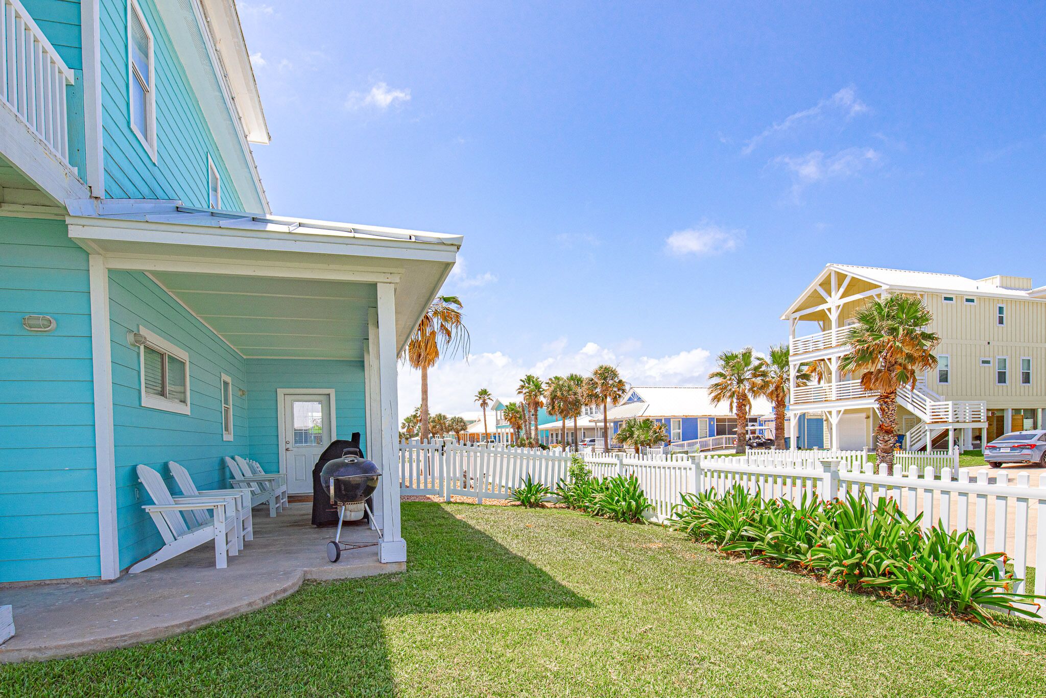 A turquoise building with a porch, white picket fence, and outdoor seating.