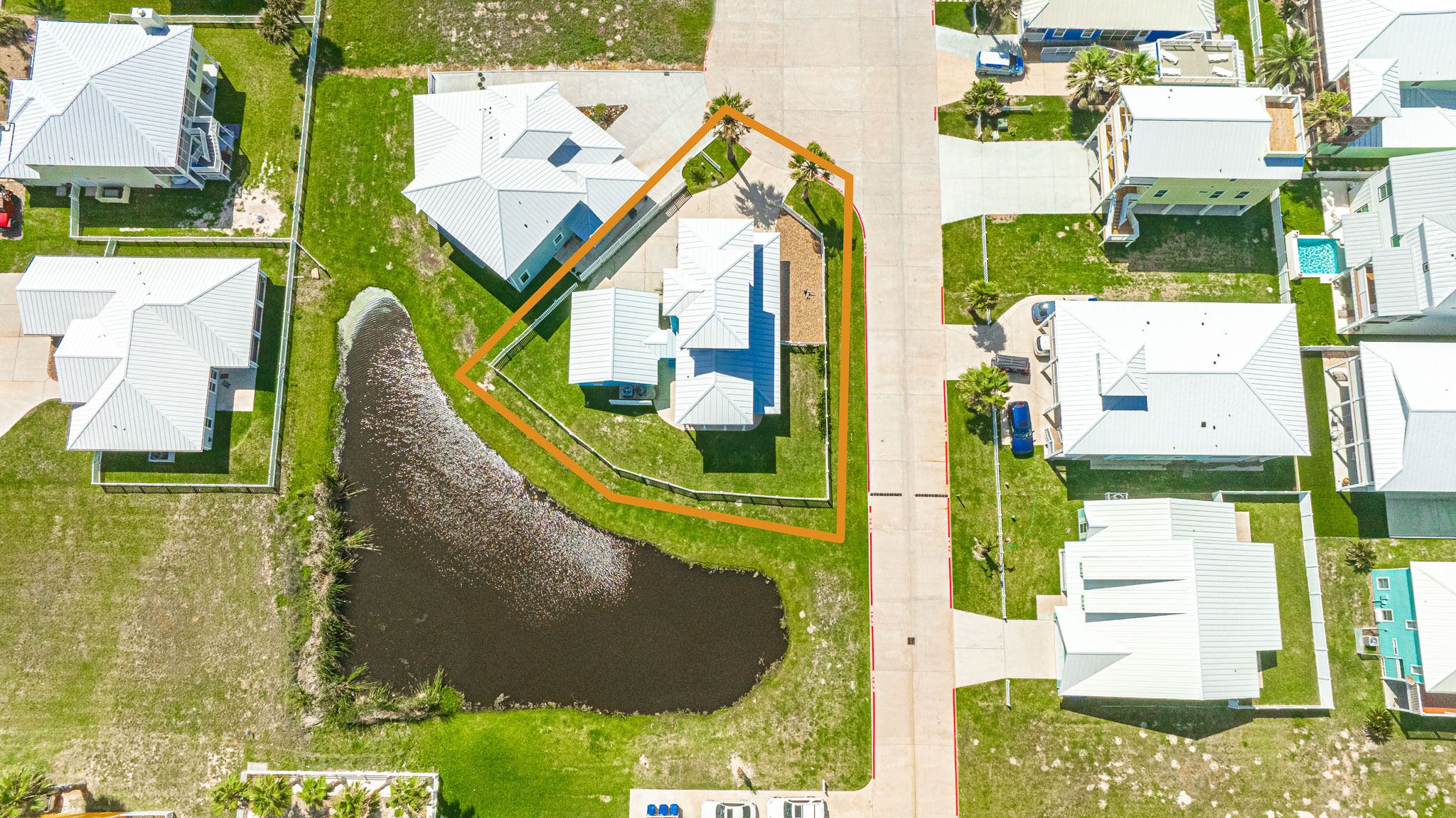 An aerial view of a residential area with multiple houses, a large pond, and a marked property boundary.