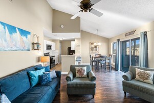 A spacious living area with a blue sofa, two armchairs, a dining table, and a kitchen in the background.