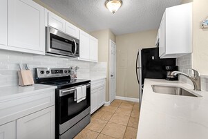 A modern kitchen with white cabinetry, a stainless steel oven, a microwave, and a black refrigerator.