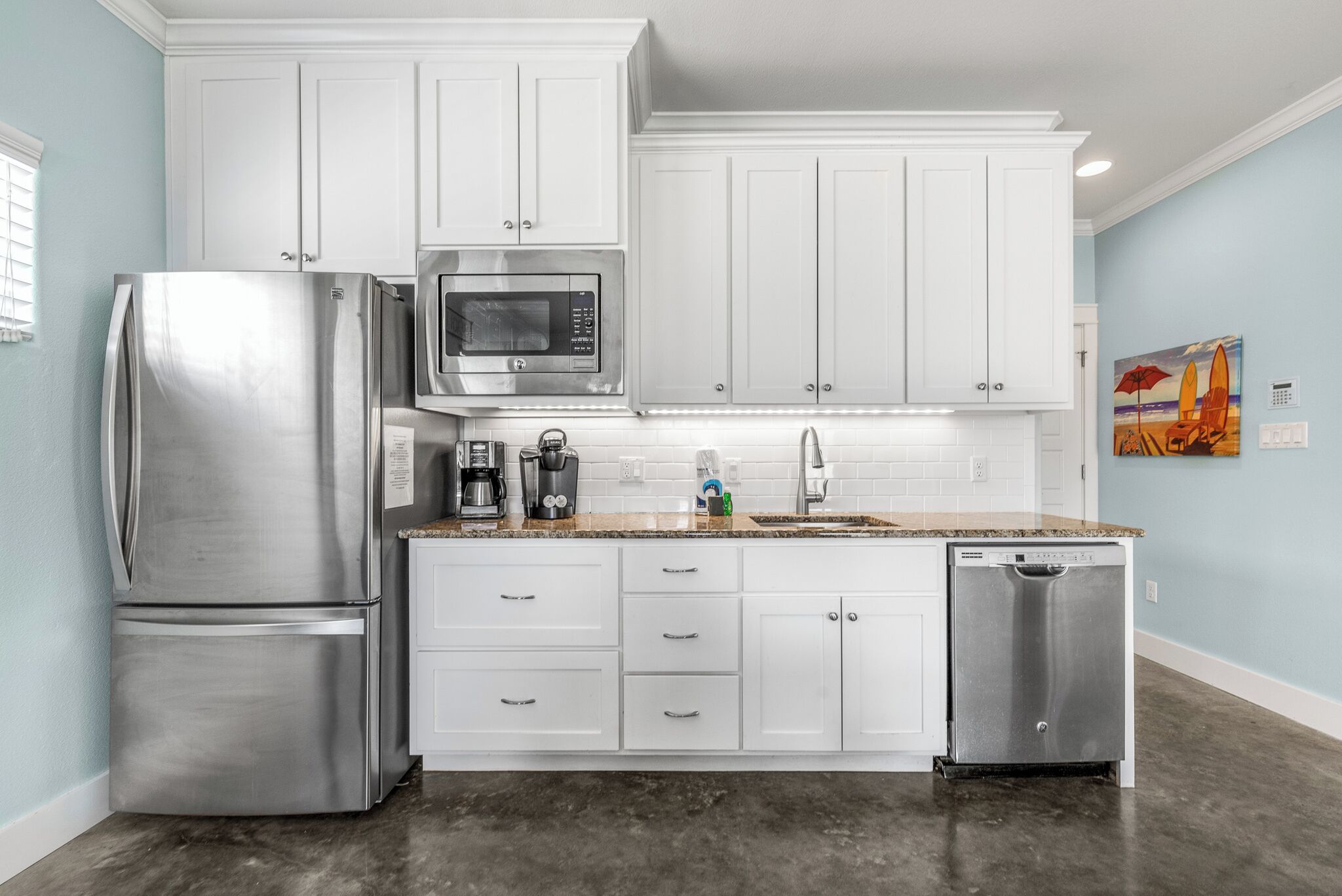 A kitchen with white cabinets, a stainless steel refrigerator, a microwave, a coffee maker, and a dishwasher.