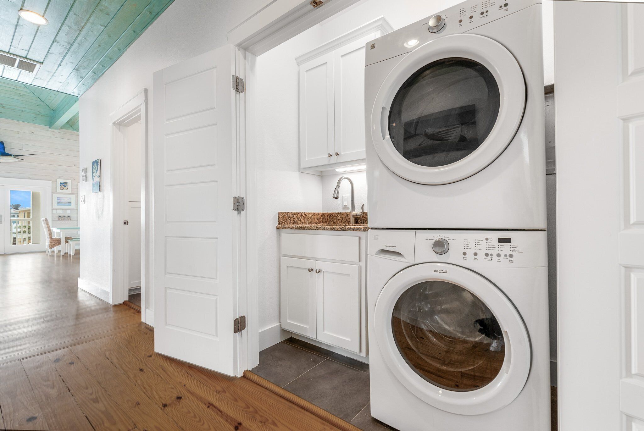 A laundry room with two front-loading washing machines, white cabinetry, and a wooden floor.