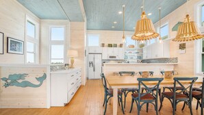 A spacious kitchen with wooden cabinets, a dining area with a wooden table and chairs, and pendant lights. - Eleventh III (Port Aransas)