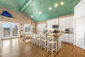 A spacious kitchen with white cabinets, a central island with bar stools, and a teal ceiling.