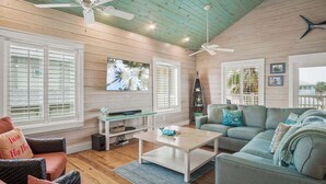 A spacious living room with wooden floors, a ceiling fan, a television, and a cozy seating area with a couch and chairs. - Eleventh III (Port Aransas)