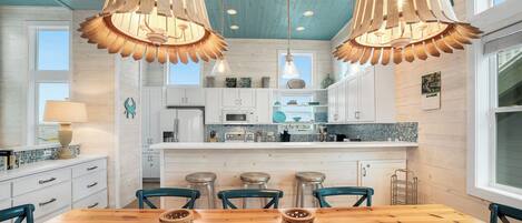 A kitchen with wooden ceiling, white cabinets, and a central island with stools.