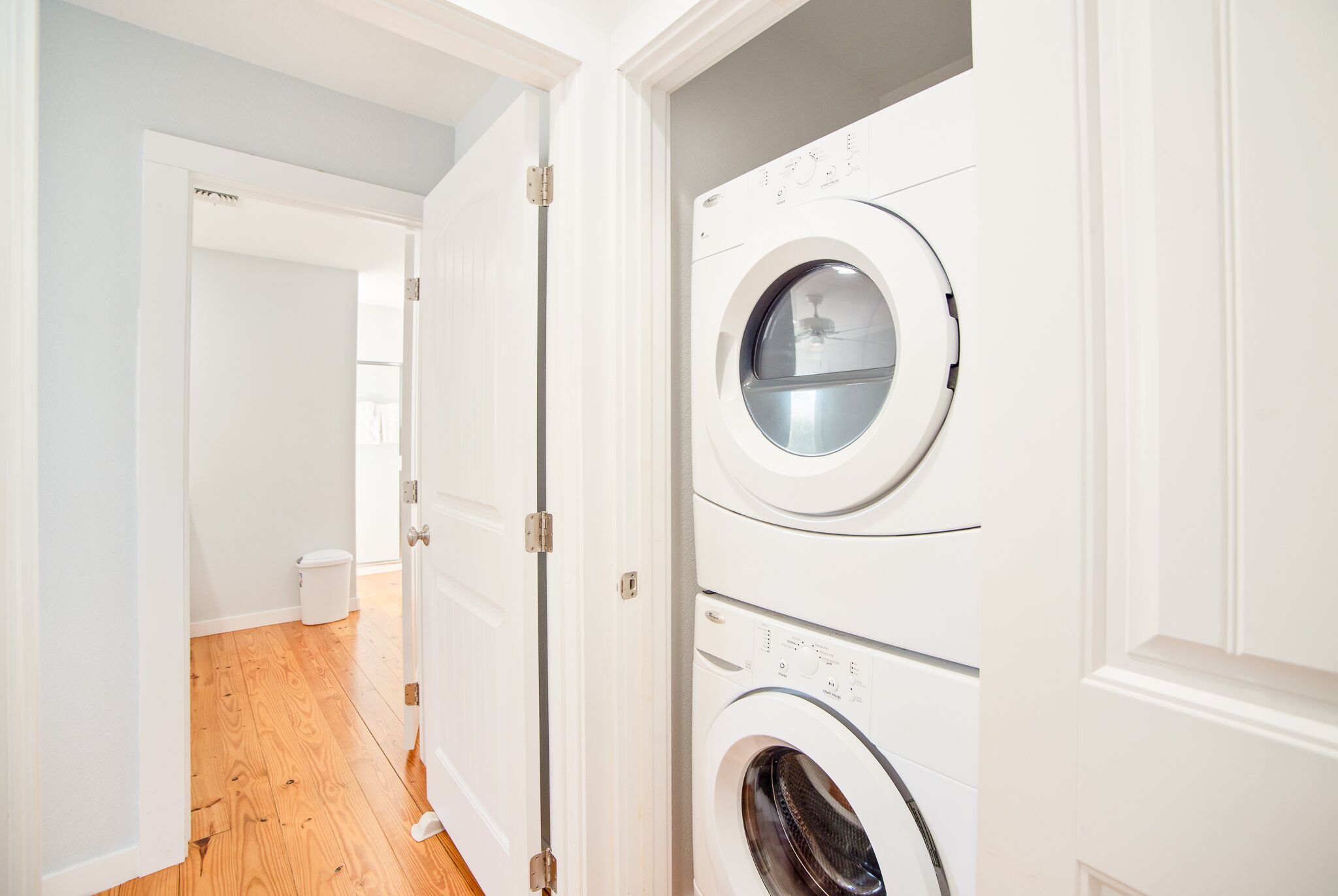 A laundry room with two stacked washers and dryers, wooden flooring, and white walls.