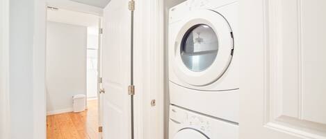 A laundry room with two stacked washers and dryers, wooden flooring, and white walls.