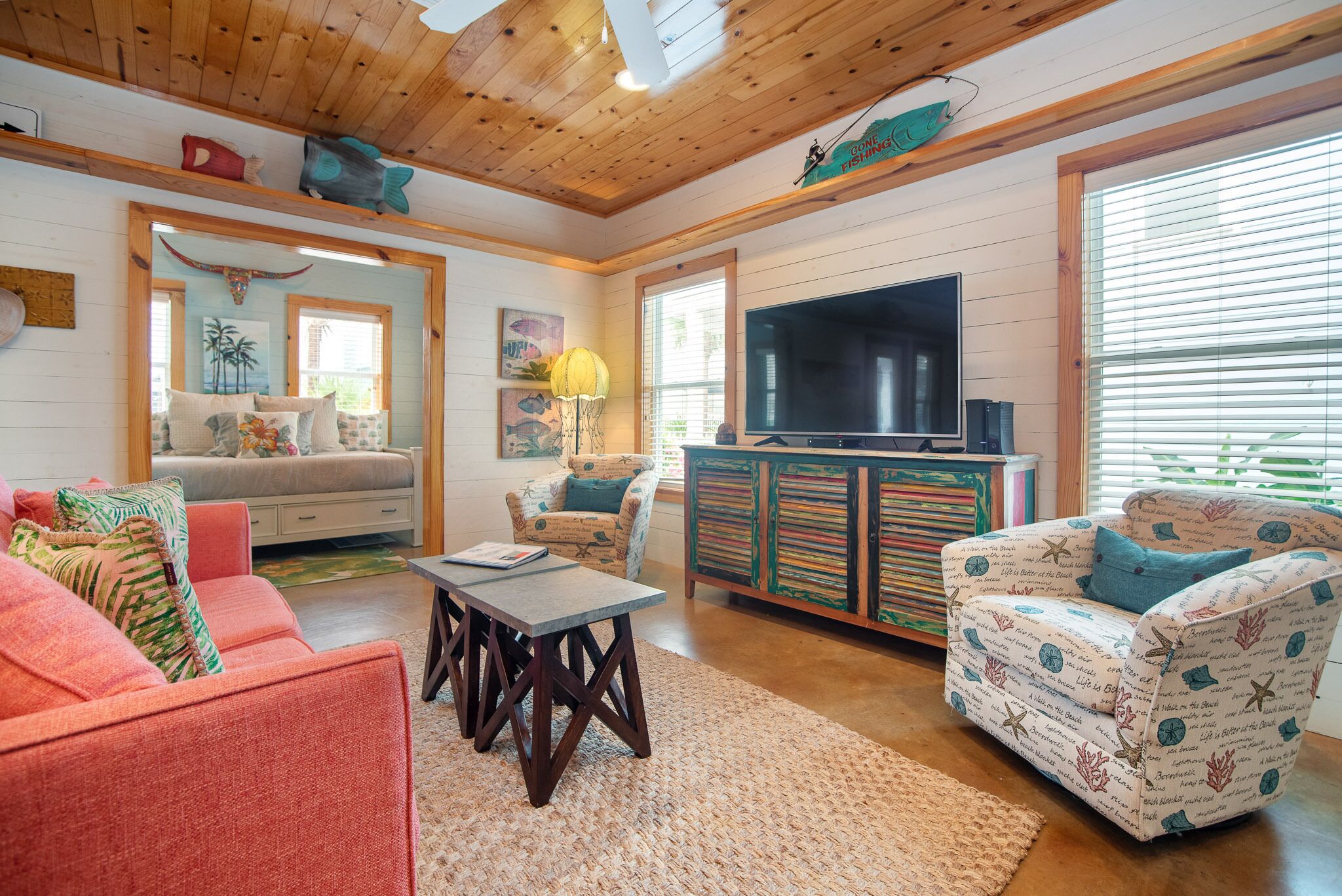 A cozy living room with a wooden ceiling, a large flat-screen TV, and a comfortable seating area with a sofa and armchairs.