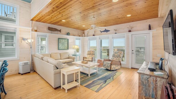 A spacious living room with a high ceiling, wooden beams, a large sofa, a coffee table, and a fireplace. - Eleventh III (Port Aransas)