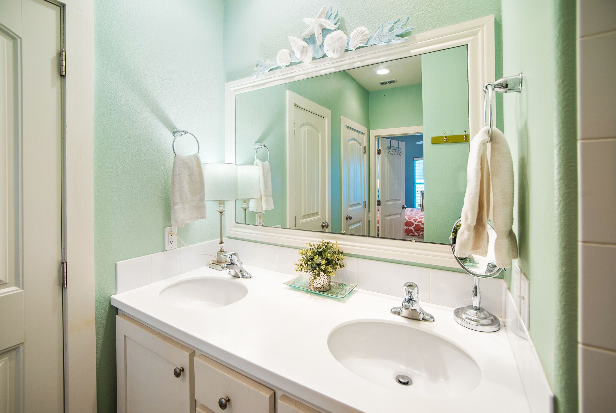 A bathroom with two sinks, a large mirror, and a decorative shell and starfish sign above the mirror.