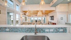A modern kitchen with a large island, pendant lights, and a view to the living area. - Eleventh III (Port Aransas)