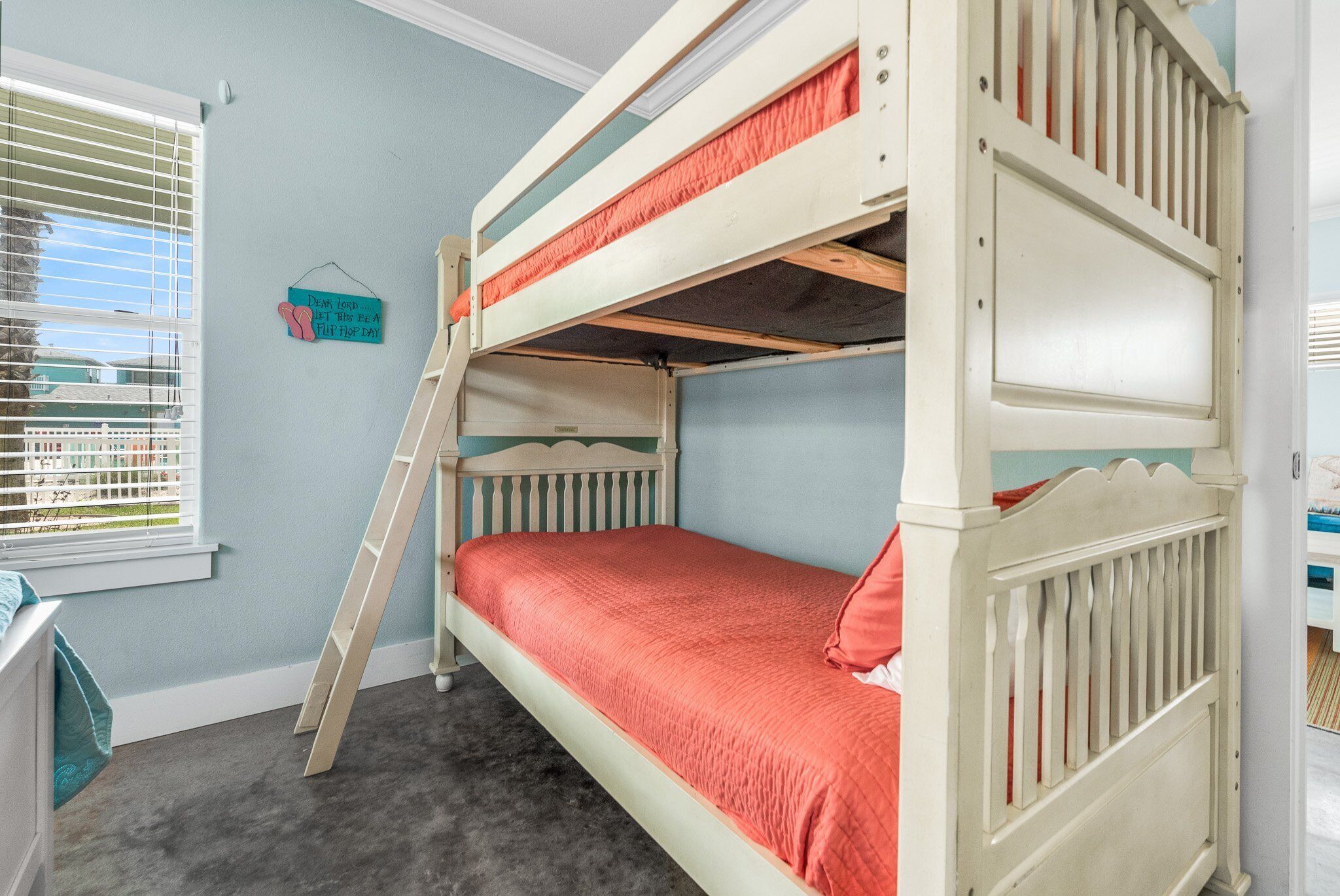 A bunk bed with a ladder, a window with blinds, and a small wall decoration.