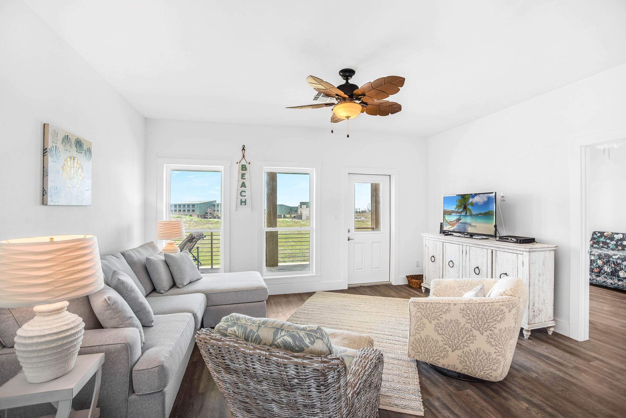 A modern living room with a grey sofa, a wicker chair, a white cabinet with a TV, and a ceiling fan.