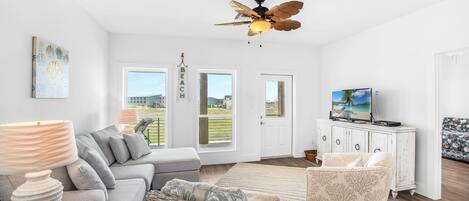 A modern living room with a grey sofa, a wicker chair, a white cabinet with a TV, and a ceiling fan.