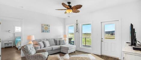 A spacious living room with a large sectional sofa, a ceiling fan, and a view of the outdoors through a door.