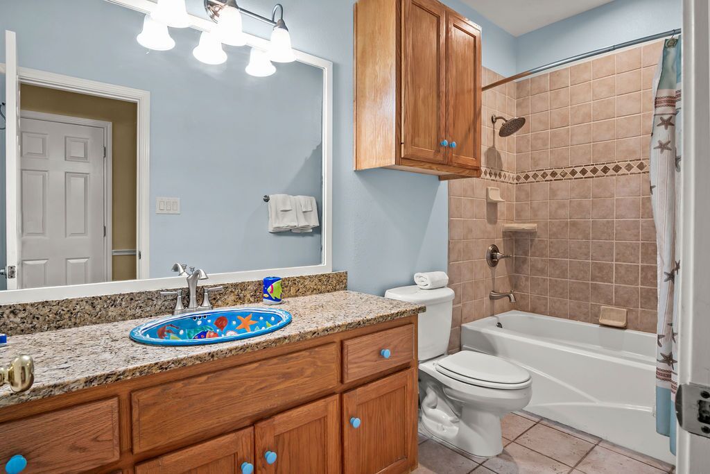 A bathroom with a sink, toilet, and bathtub. There are wooden cabinets and a mirror above the sink.