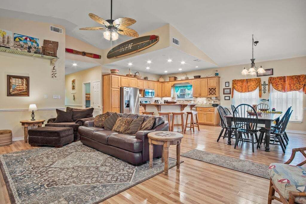 A spacious living area with a brown leather sofa, a dining table with chairs, and a kitchen in the background.