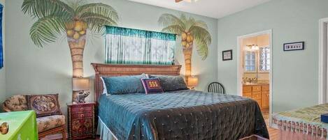 A bedroom with a bed, a nightstand, a chair, a desk, a ceiling fan, and a window with curtains.