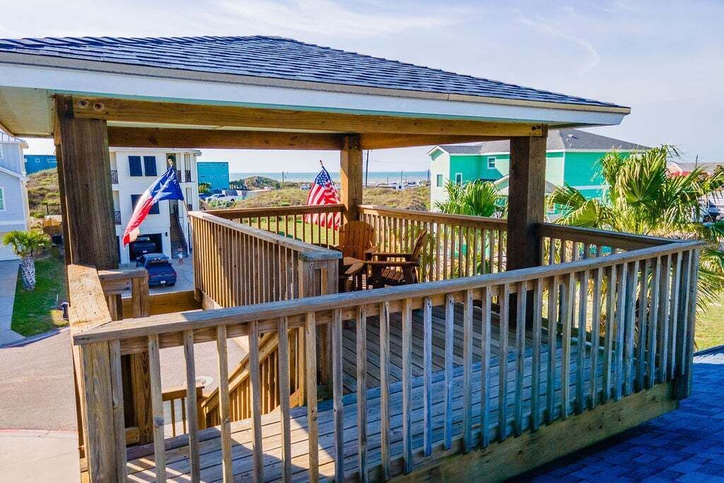 A wooden deck with a covered area, two American flags, and a view of a residential area with houses and greenery.