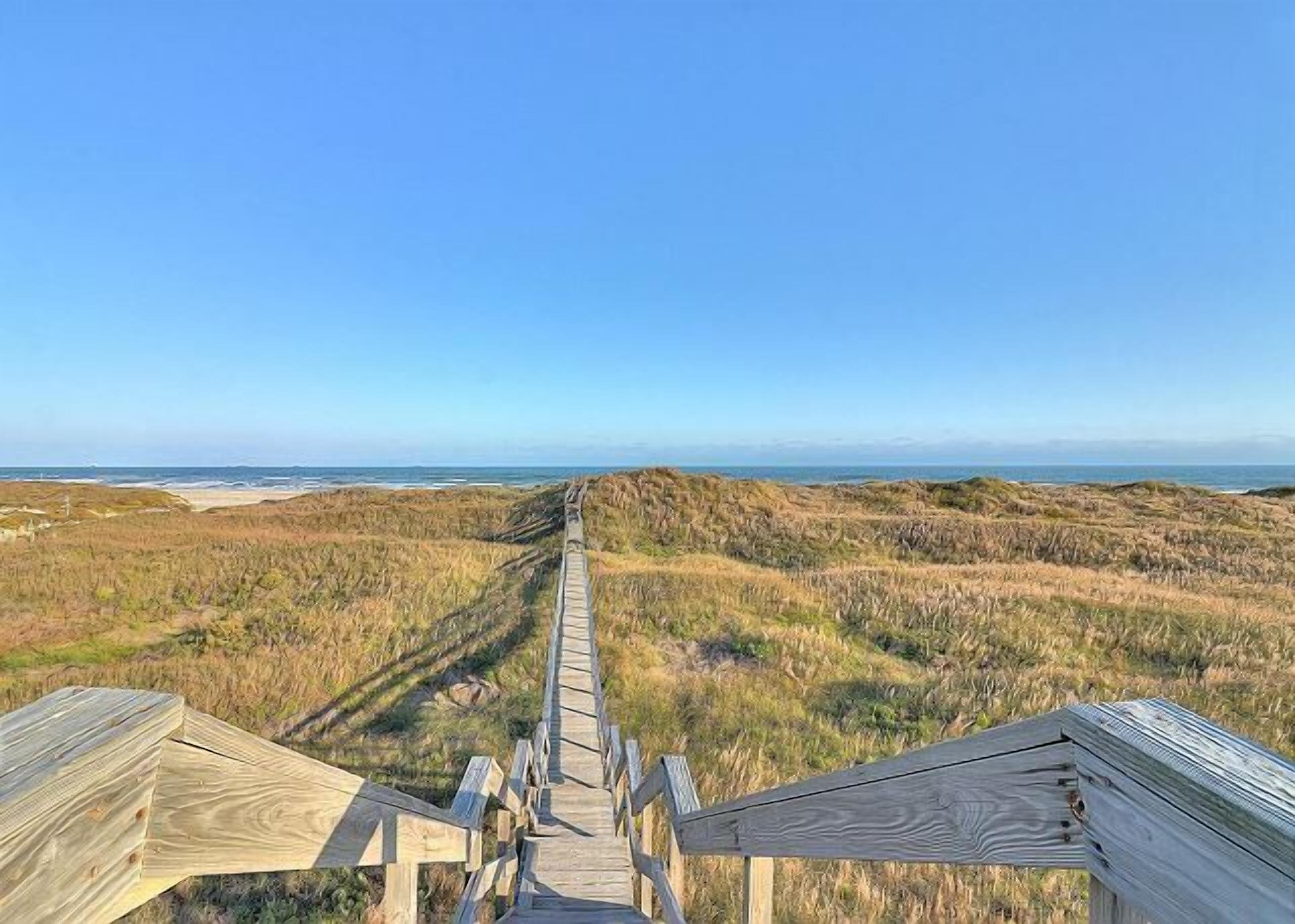 A wooden boardwalk leading to a beach with dunes and the ocean in the background.