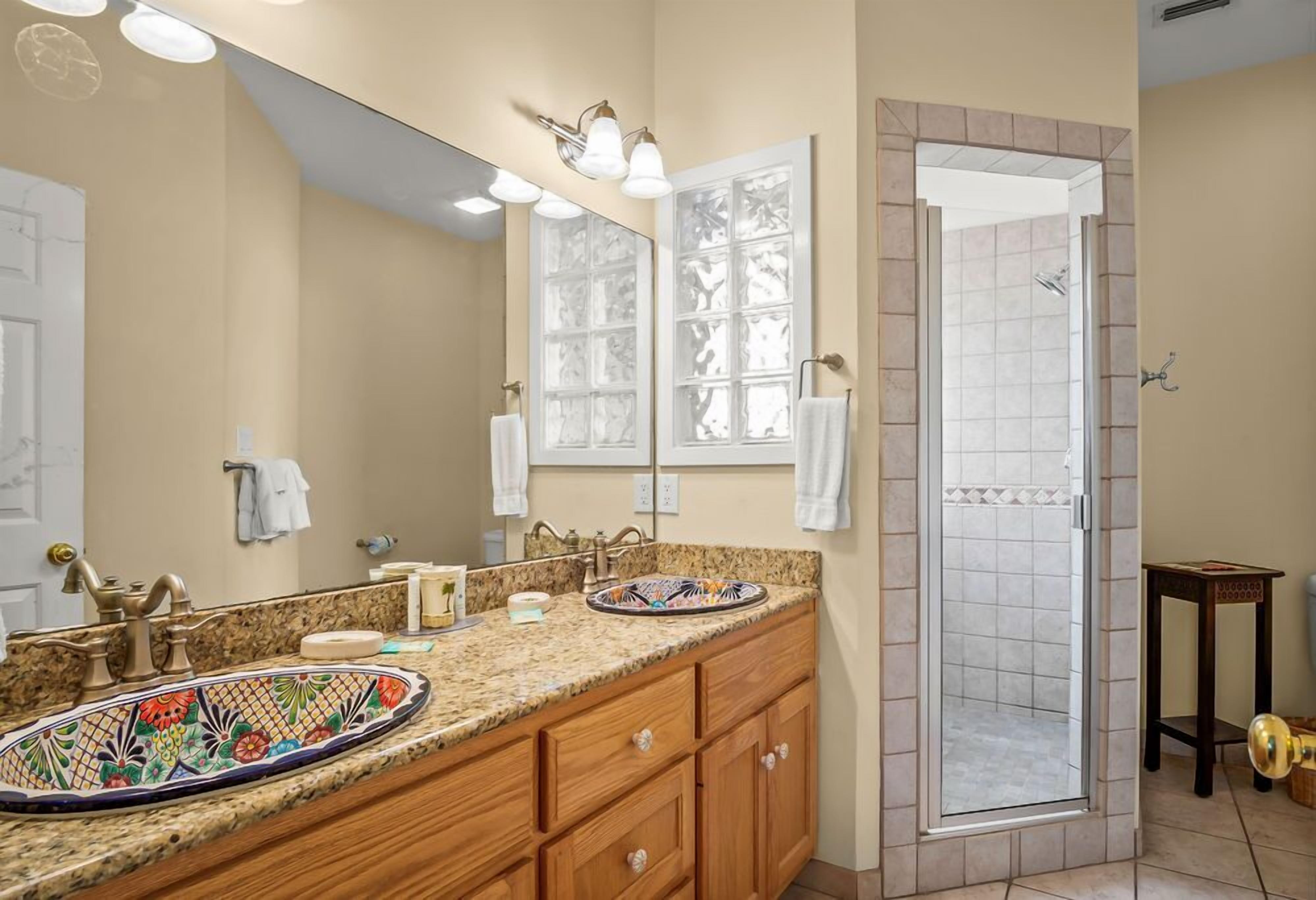 A bathroom with a double sink vanity, a large mirror, a shower enclosure, and a small table.