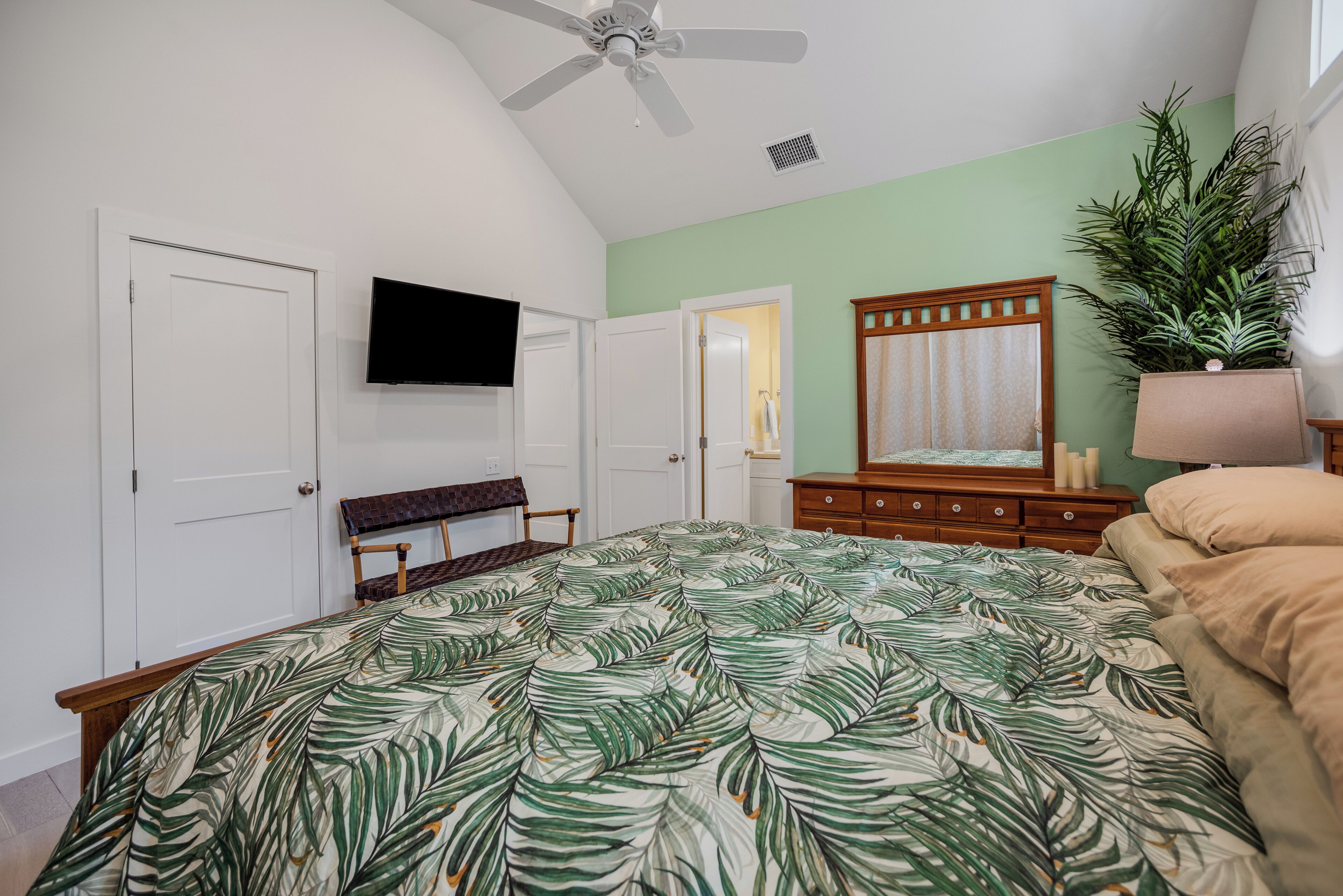 A bedroom with a bed, a television, a dresser, a bench, and a potted plant.