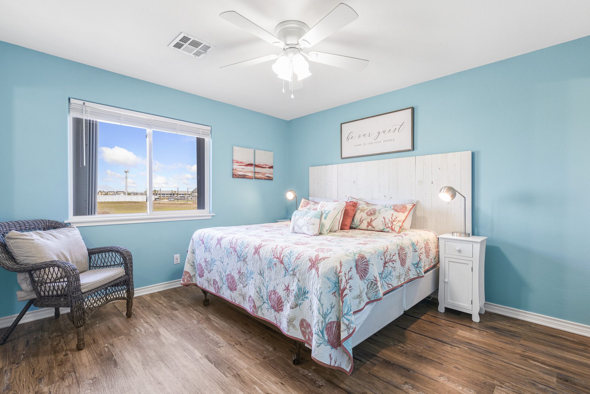 A bedroom with a bed, a chair, a nightstand, a ceiling fan, and a window with a view.