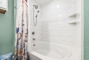 Un baño con una bañera blanca, ducha con cabezal de ducha de mano y cortina con motivos náuticos.