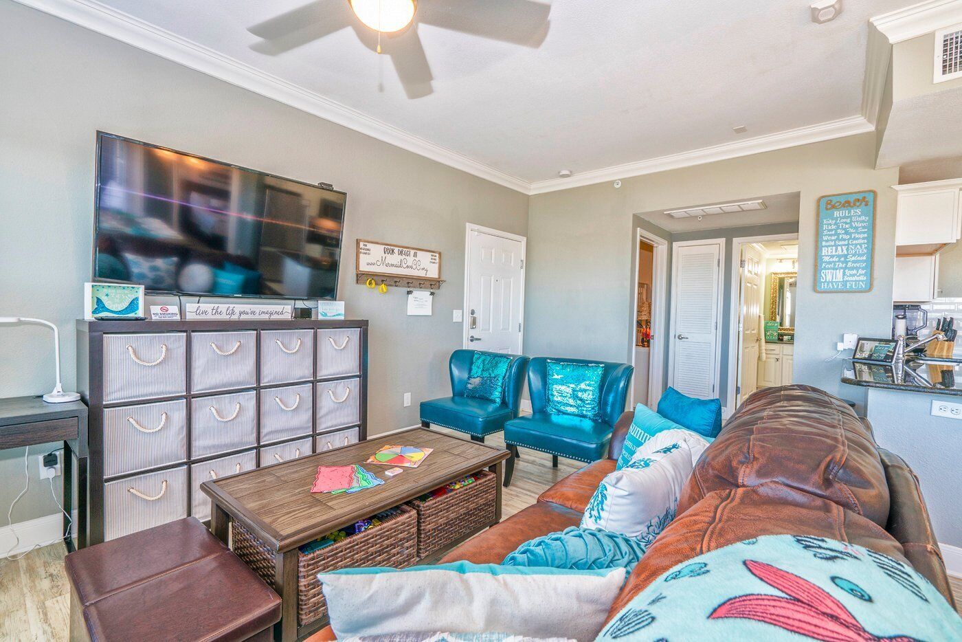 A living room with a TV, a coffee table with a map, a bookshelf, and two blue armchairs.