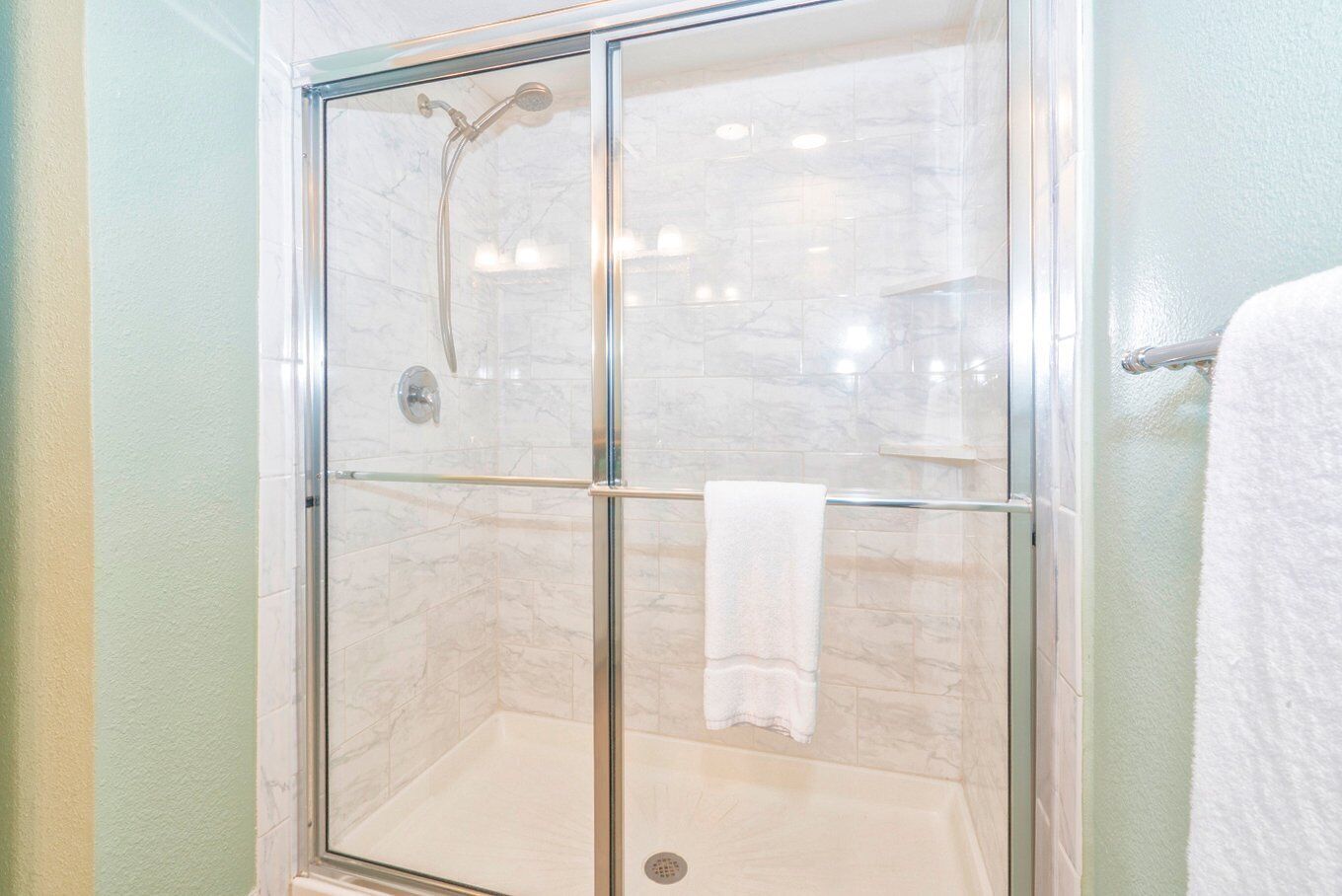 A glass-enclosed shower with a glass door and a towel rack.