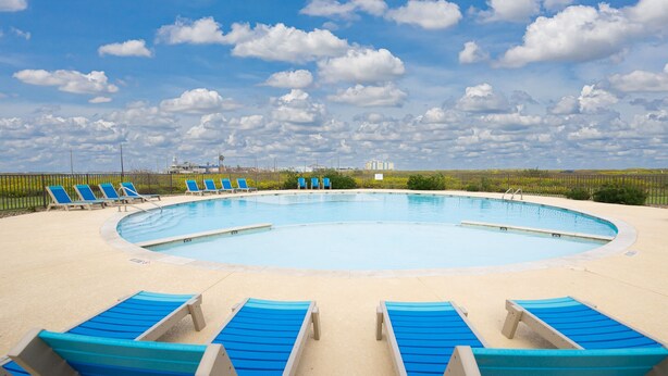 Una piscina circular con sillas reclinables azules alrededor, cielo despejado y edificios a lo lejos.